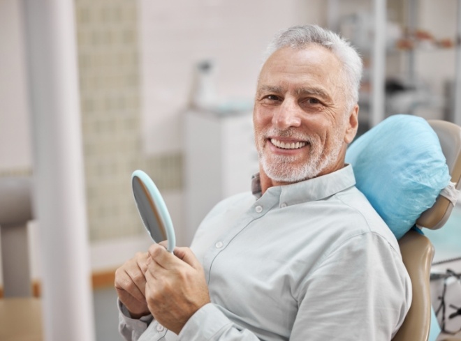 Senior man holding mirror and smiling in dental chair