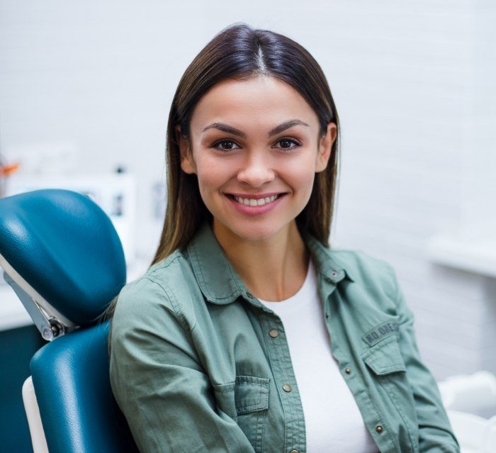 Young woman in green jacket smiling while visiting cosmetic dentist in Houston