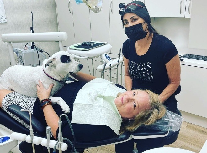 Doctor Alani next to therapy dog lying on top of patient in dental chair