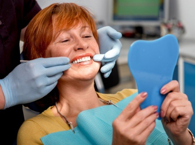 Older redheaded woman in dental chair admiring her new smile in mirror