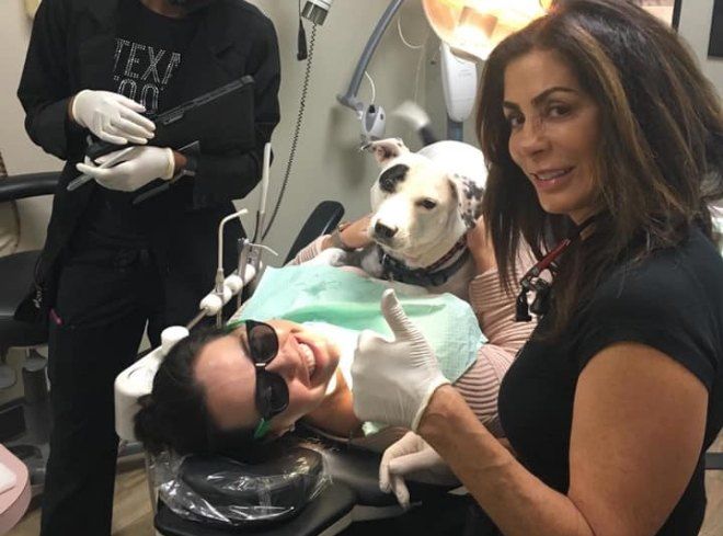 Doctor Alani giving thumbs up next to therapy dog lying on dental patient