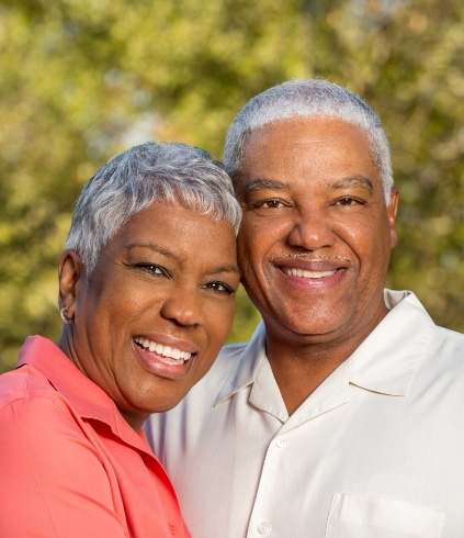 Senior man and woman smiling together with trees in background