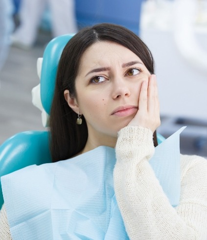 Woman in dental chair holding her cheek in pain