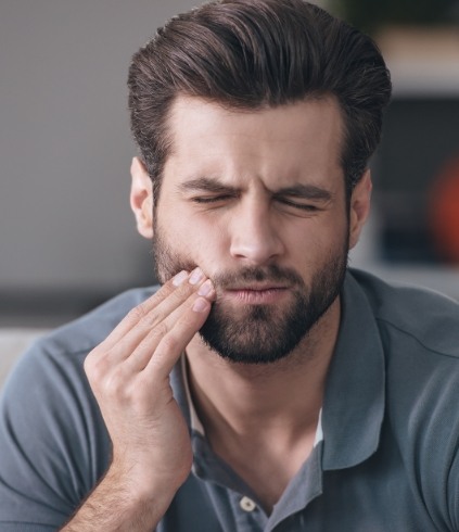 Man in gray polo shirt holding his jaw in pain