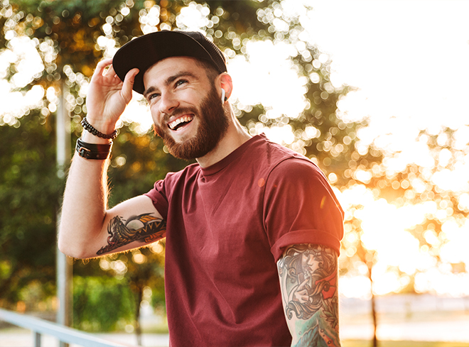 Young man with tattoo sleeves smiling outdoors at sunset