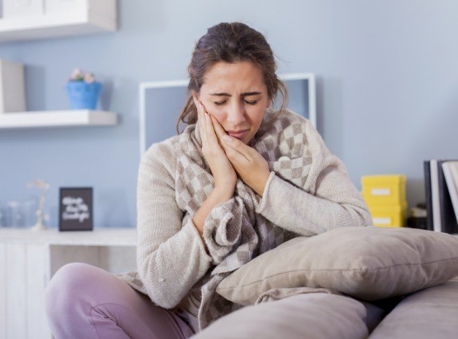 Woman sitting on couch holding her cheek in pain