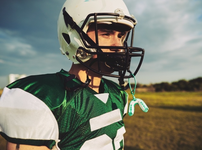 Football player with athletic mouthguard hanging from their helmet