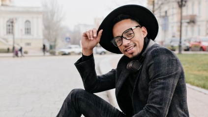 Man in black suit and black wide brimmed hat sitting on sidewalk