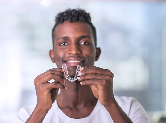 Smiling man holding Invisalign clear aligner