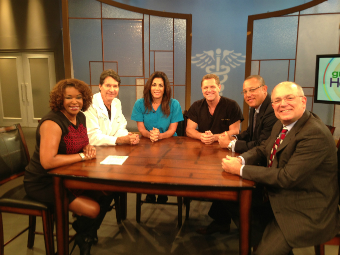 Doctor Alani sitting at table with several other medical professionals on T V show