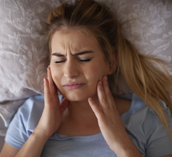 Woman laying in bed and touching her face in pain