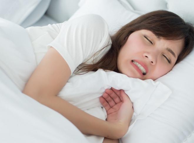 Woman cringing in pain while lying in bed