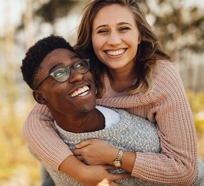 Man and woman in sweaters laughing together outdoors after smile makeover in Houston