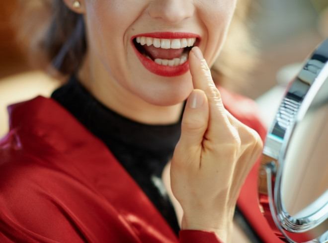 Woman in red lipstick looking at her teeth in mirror