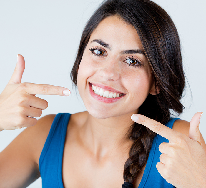 Woman pointing to her smile after teeth whitening in Houston
