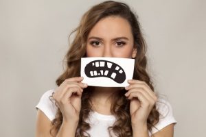 A woman holding an illustration of a crooked smile over her mouth.