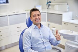 Man smiling and holding thumbs up at dentist